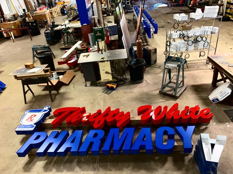 Sign for The Fifty White Pharmacy in progress, red and blue letters in a workshop. Sign for The Fifty White Pharmacy in progress, red and blue letters in a workshop.