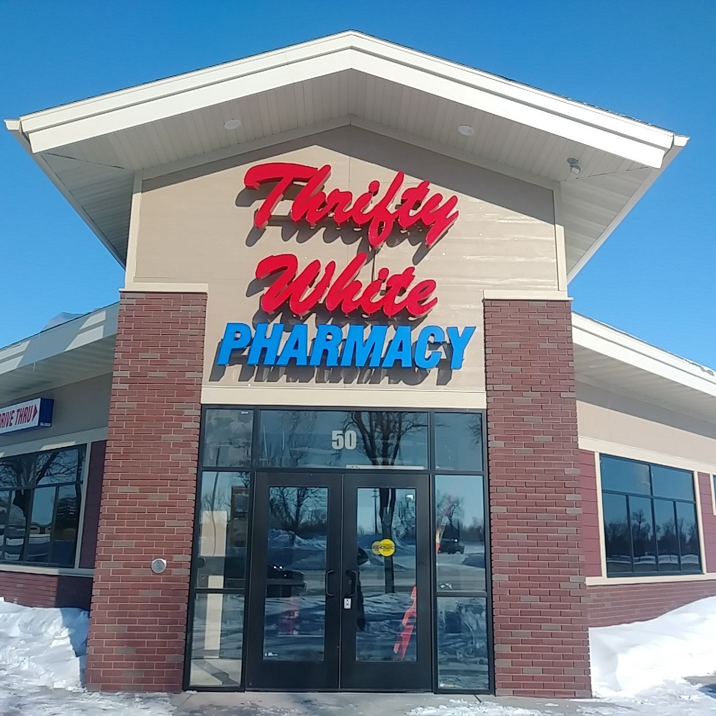 Thrifty White Pharmacy storefront with red and blue sign, brick and glass facade, snow on the ground. Thrifty White Pharmacy storefront with red and blue sign, brick and glass facade, snow on the ground.
