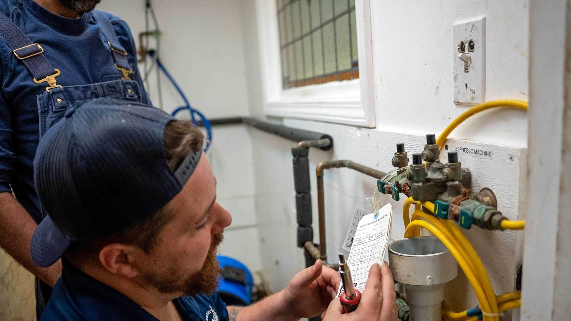 Technician inspecting gas valves and yellow hoses on a wall-mounted meter in a utility room