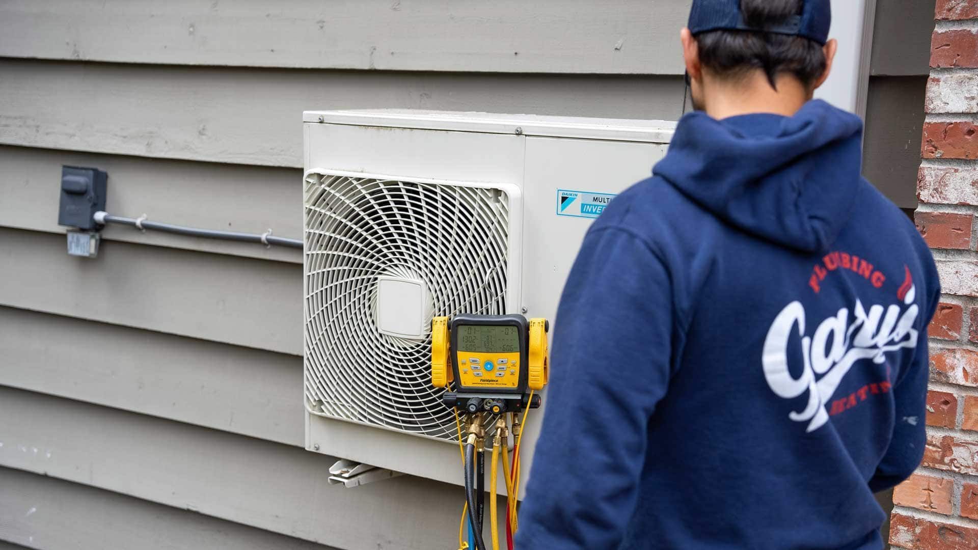 Technician inspecting outdoor air conditioner unit with yellow diagnostic meter on a house exterior