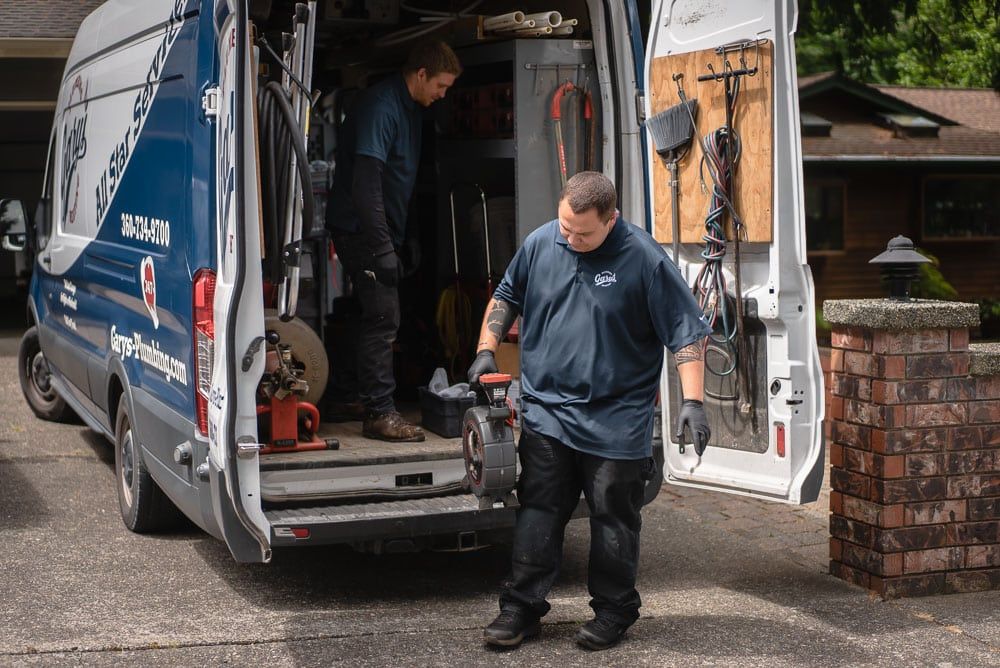 Gary's Plumbiing and Heating technician unloading equipment from a blue van on a residential street
