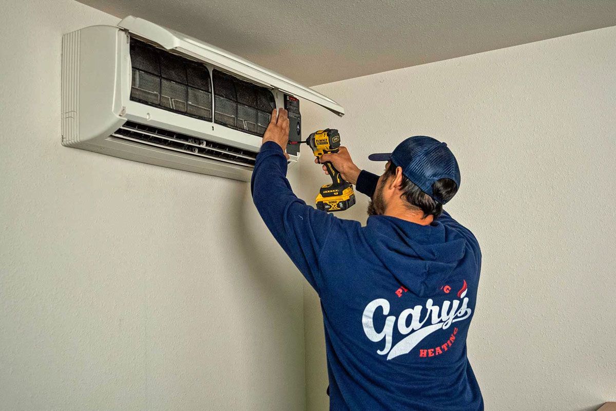 Technician cleaning a wall-mounted air conditioner with a drill attachment indoors