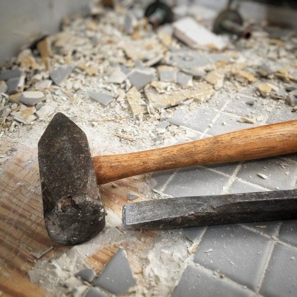 Hammer and chisel on a dusty surface with broken gray tiles and debris