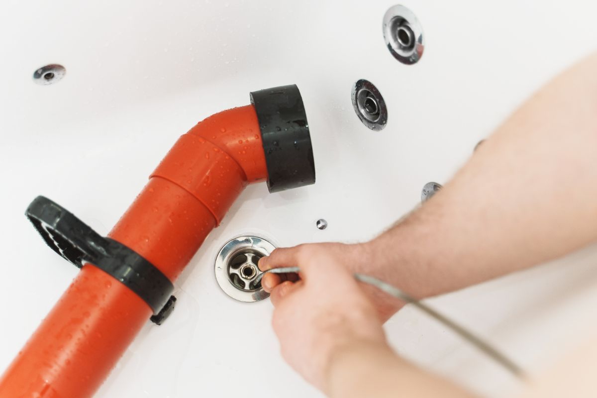 Hands installing a red pipe fitting on a white bathtub drain assembly