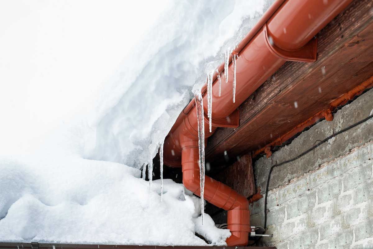 Icicles hanging from a red gutter above a snow-covered roof and gray wall