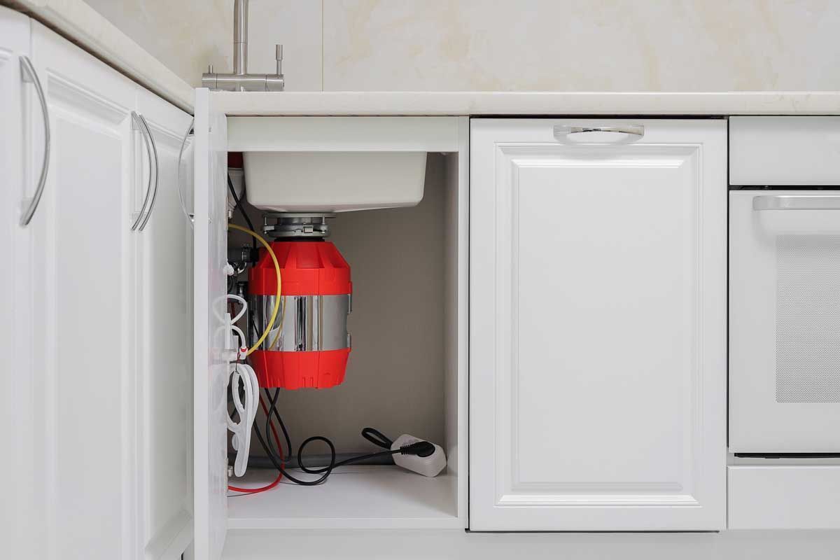 Under-sink cabinet with a red fire extinguisher and cleaning supplies next to a washing machine