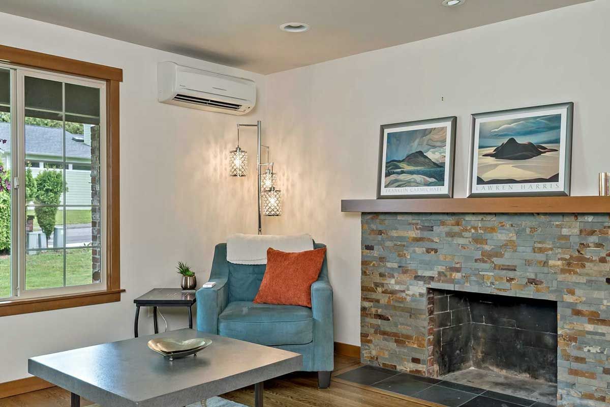 Cozy living room with blue chair, coffee table, stone fireplace, and framed seascape art.