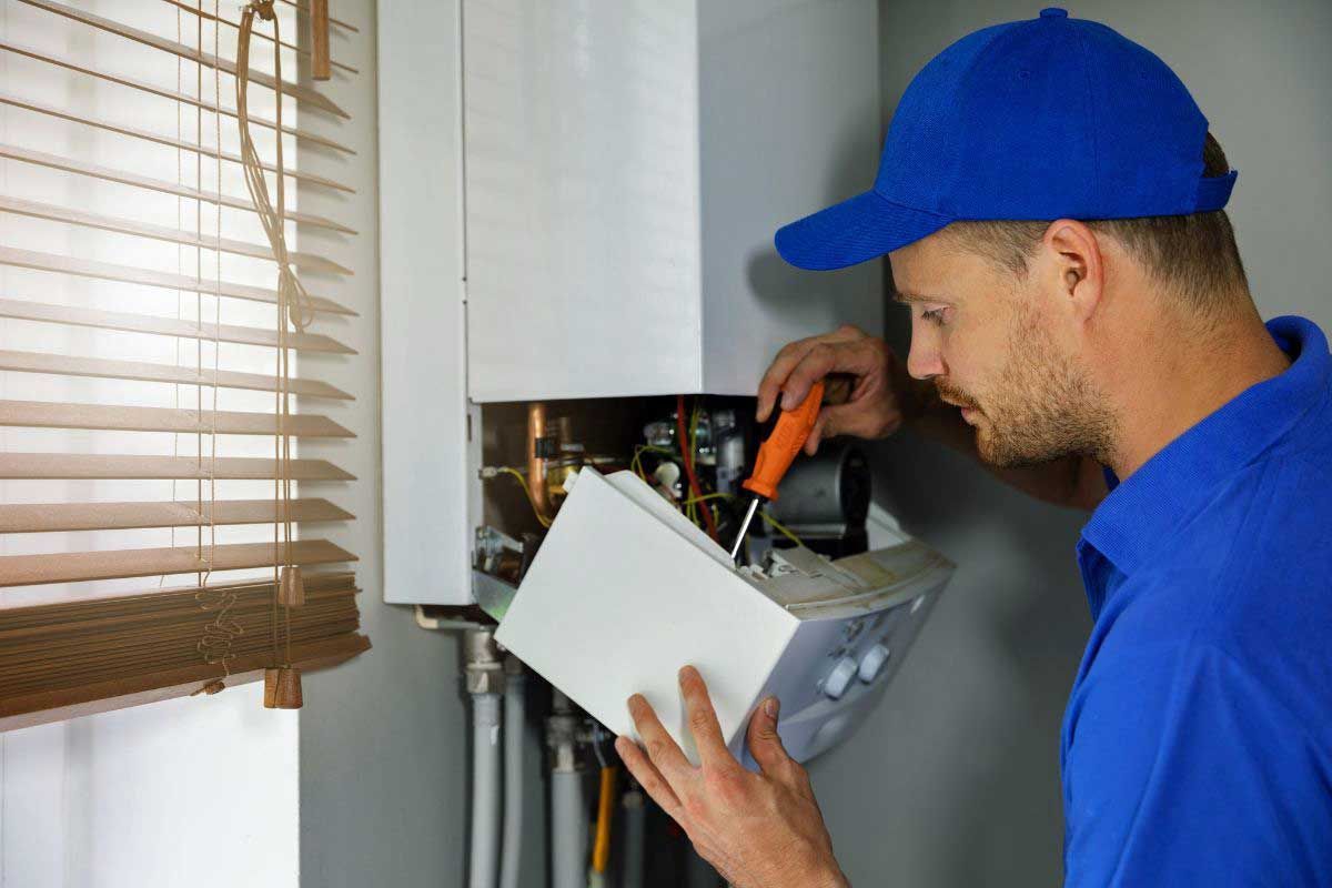 Technician in blue cap and shirt inspecting an electrical panel beside a window