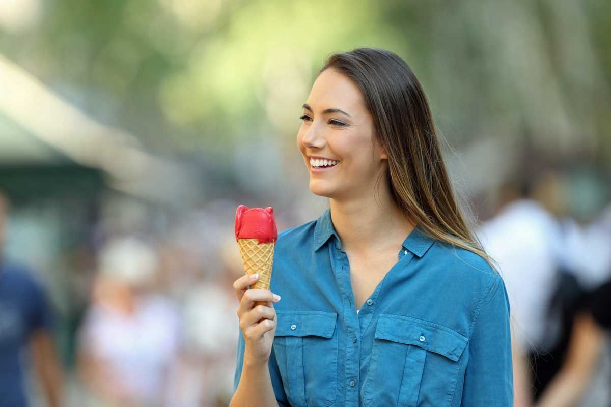 Woman smiling and holding a red and yellow ice cream cone outdoors