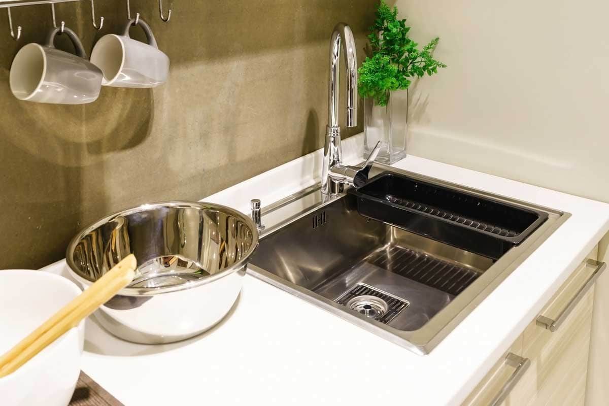 Modern kitchen sink with dish rack, bowl, chopsticks, hanging mugs, and small plant on countertop
