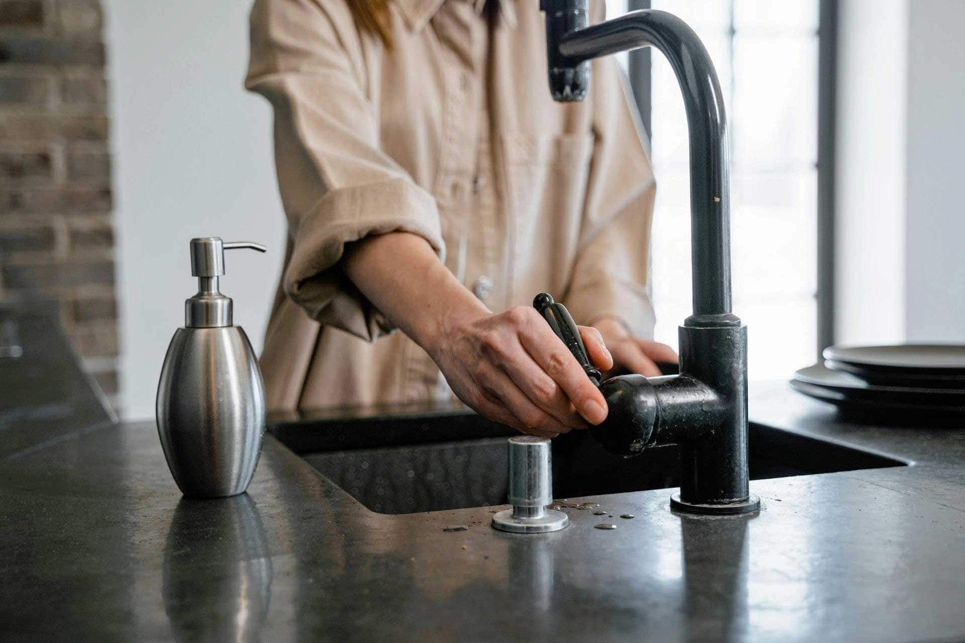 A woman closing a black faucet in a kitchen sink