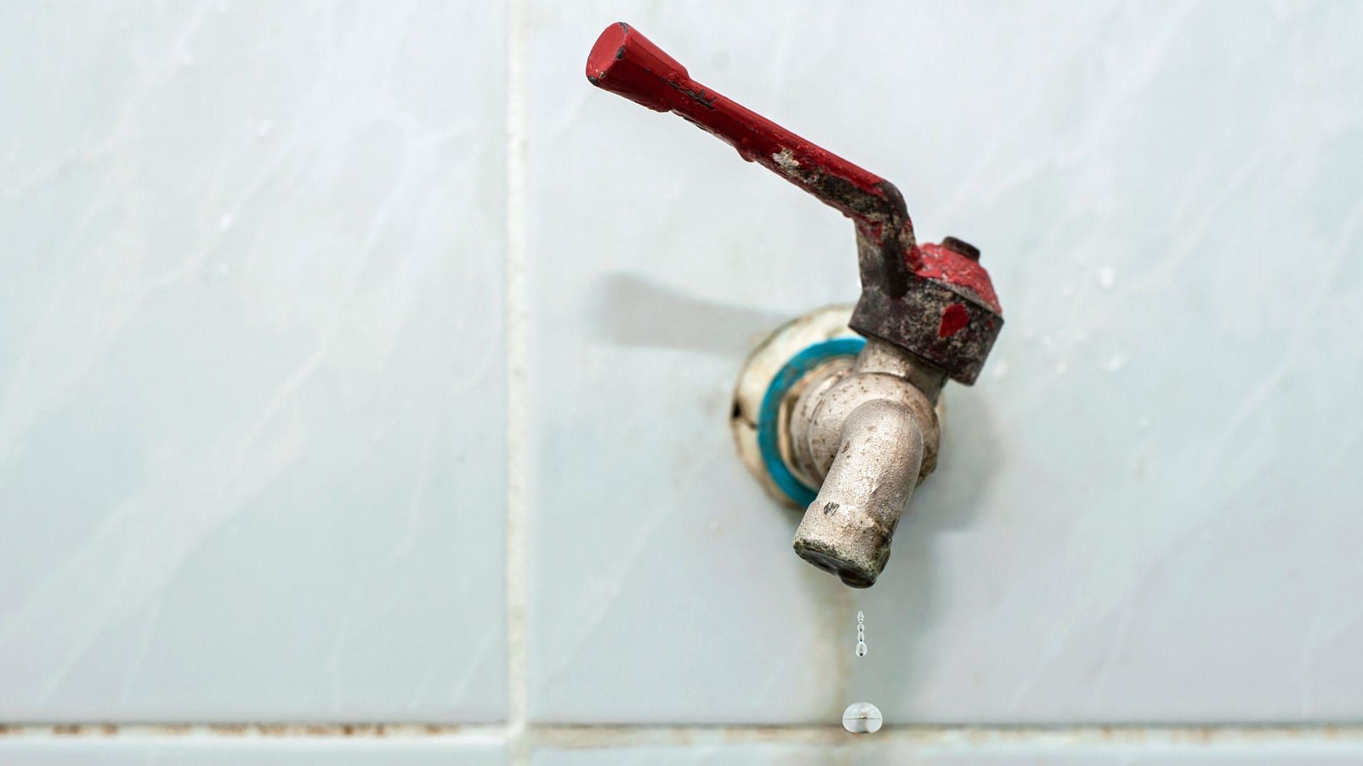 Leaking outdoor faucet with a red handle on a tiled wall