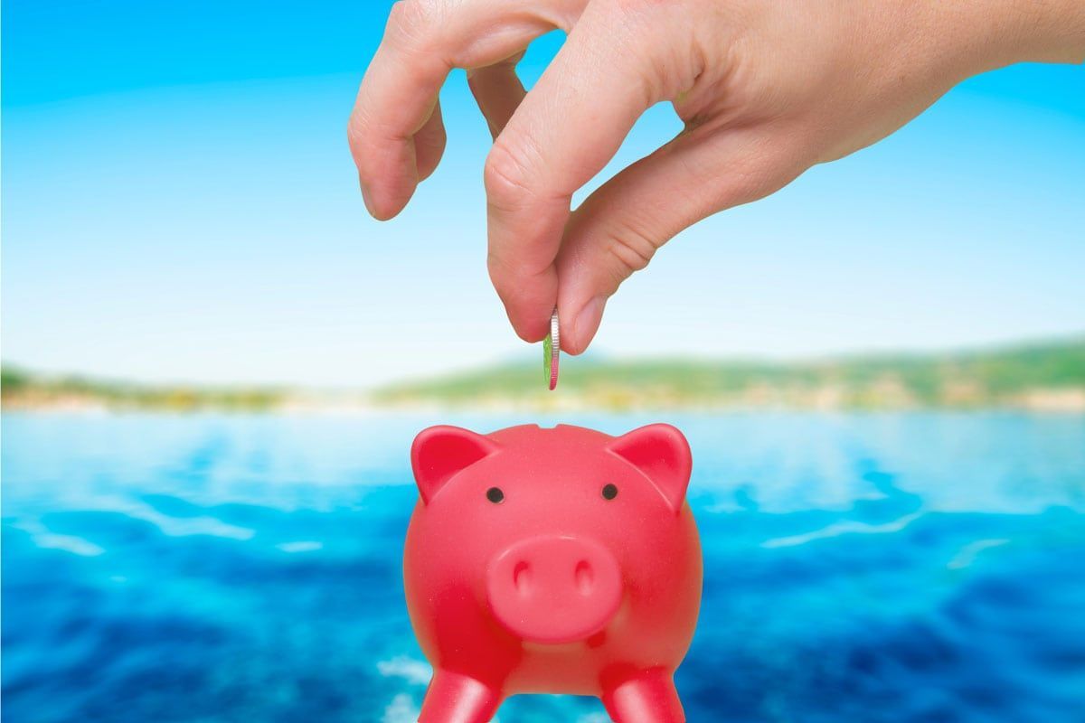 Hand placing a coin into a pink piggy bank with blue water in the background