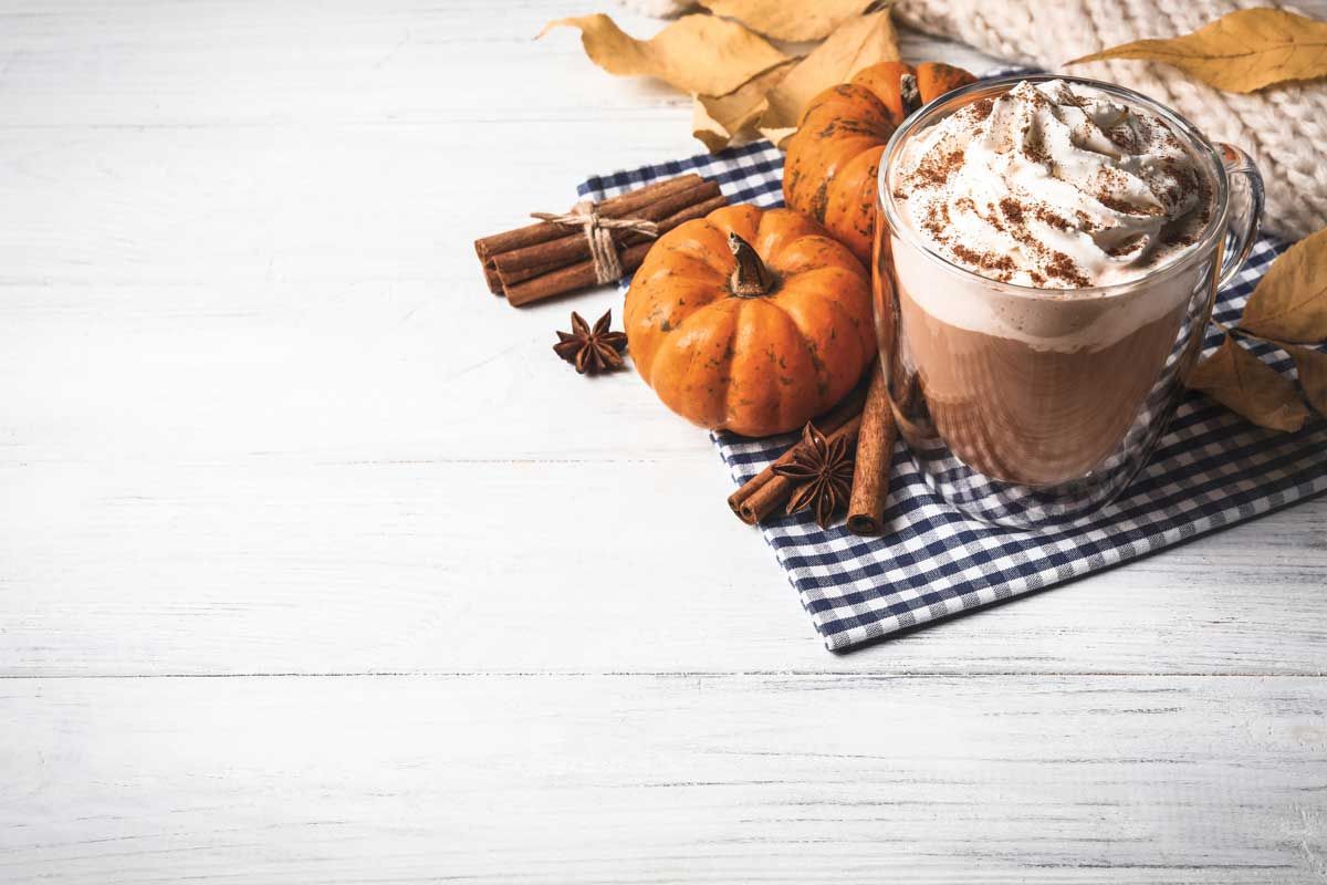 Pumpkin spice latte with pumpkins and cinnamon on a checkered napkin on a white wooden table
