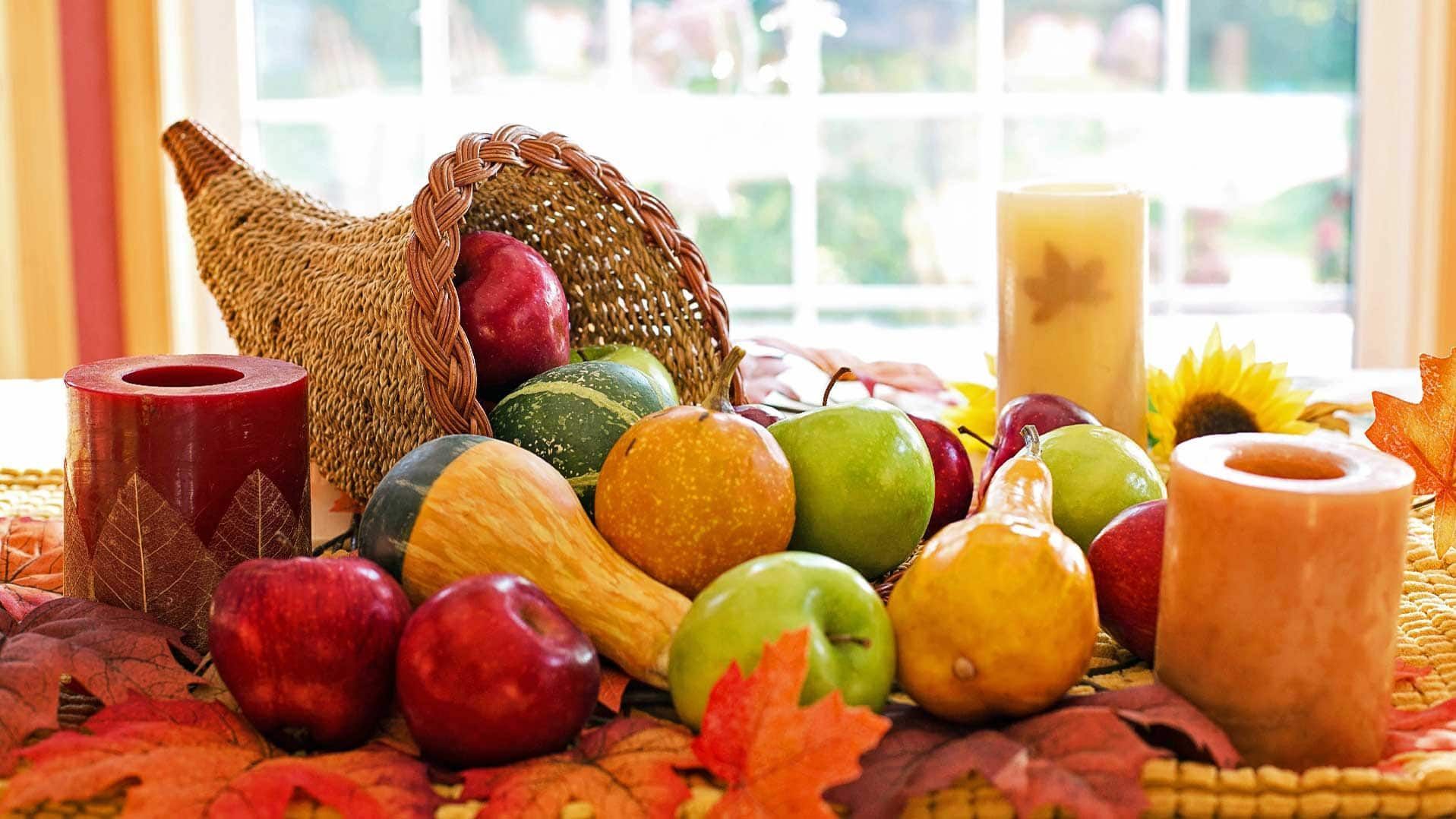 Harvest display with apples, pumpkins, gourds, autumn leaves, candles, and a cornucopia on a table.