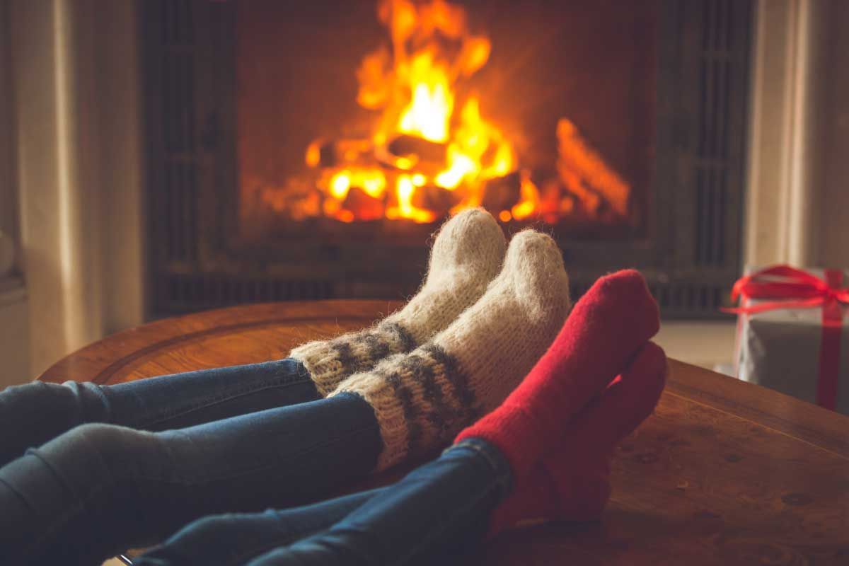 Two pairs of feet in socks by a glowing fireplace, with a wrapped gift on the side