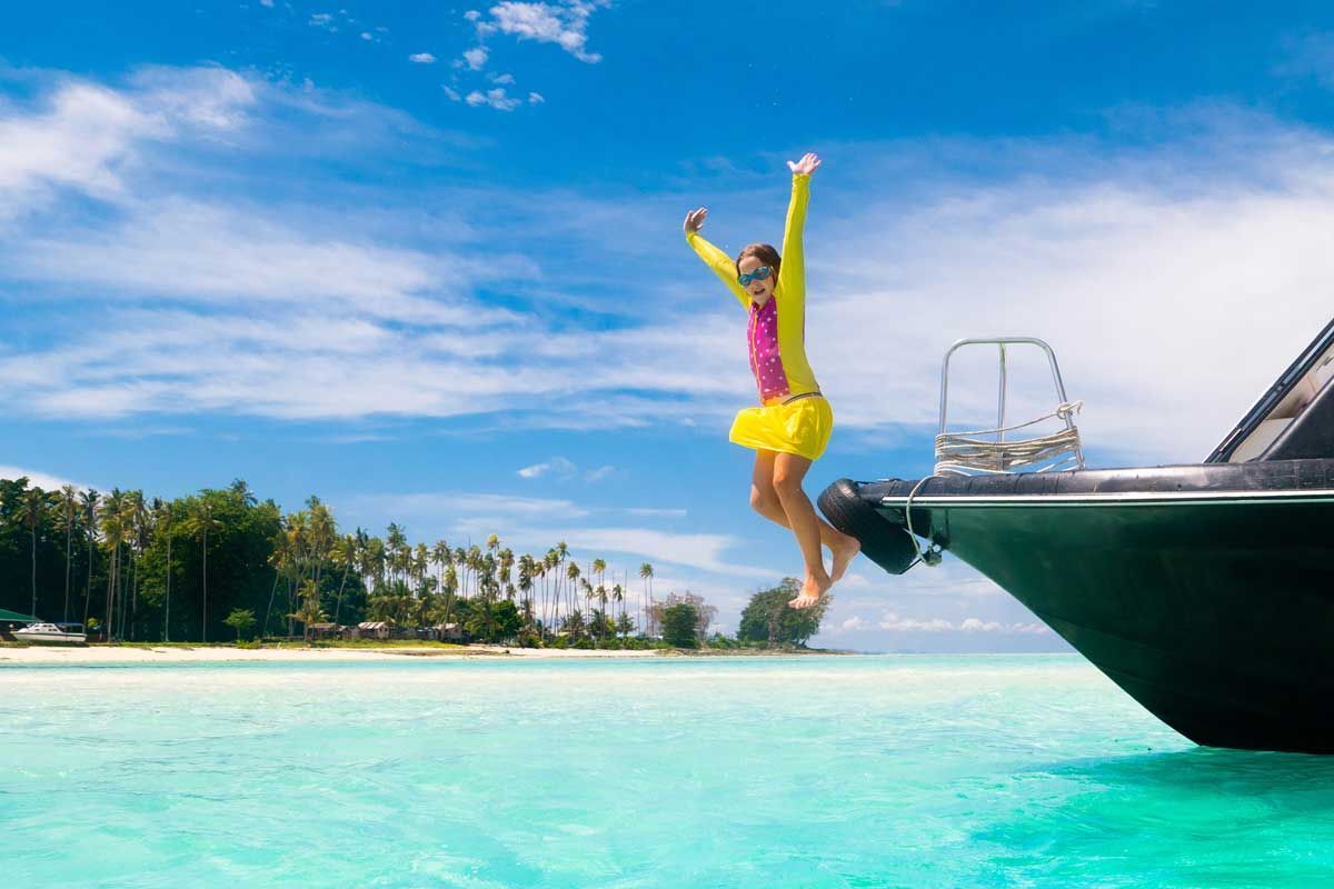 Person in yellow swimsuit jumps from a boat into bright turquoise tropical water.
