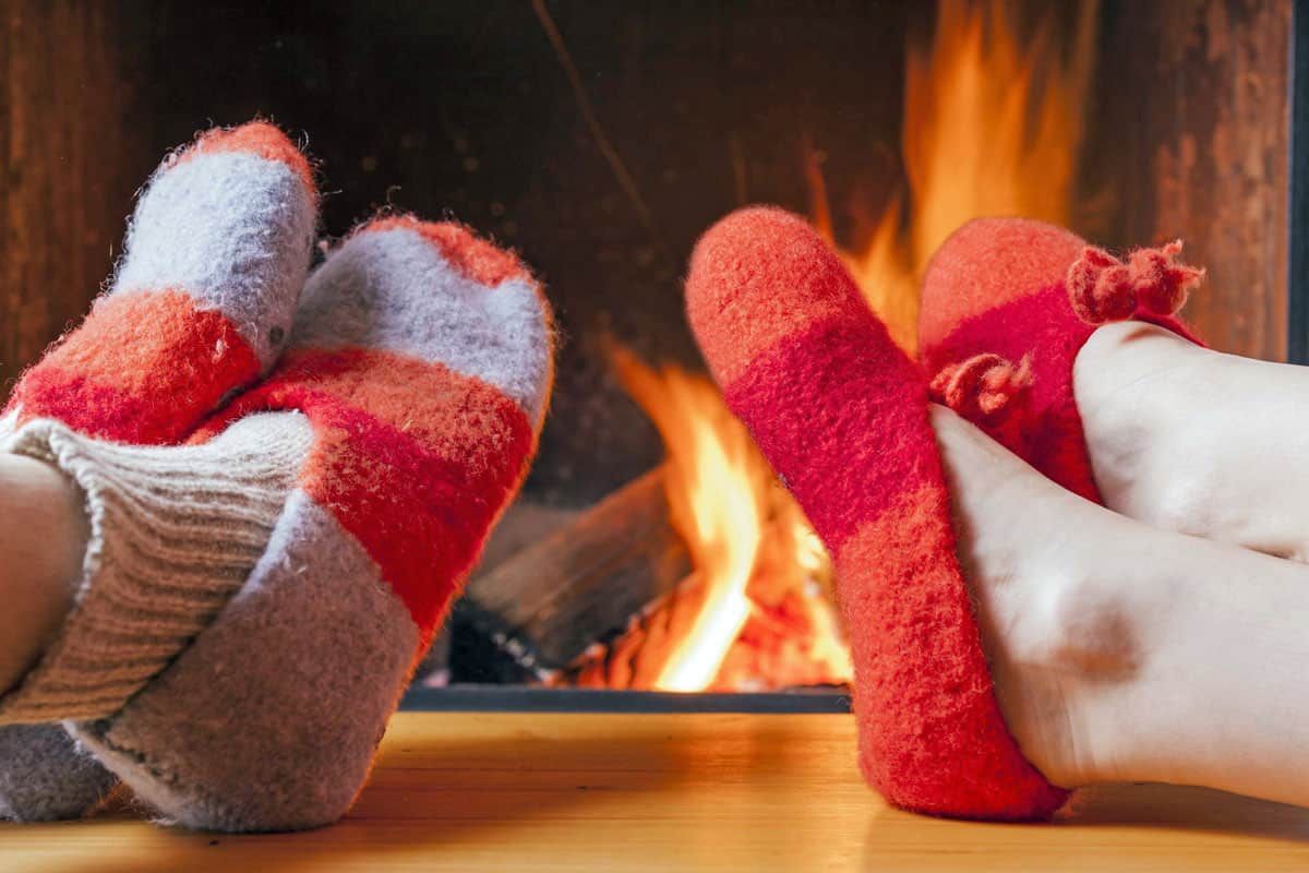 Two pairs of socked feet warming by a cozy fireplace, with orange flames in the background