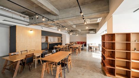 A modern cafe with wooden tables, shelves, and a pegboard wall under industrial ceiling.