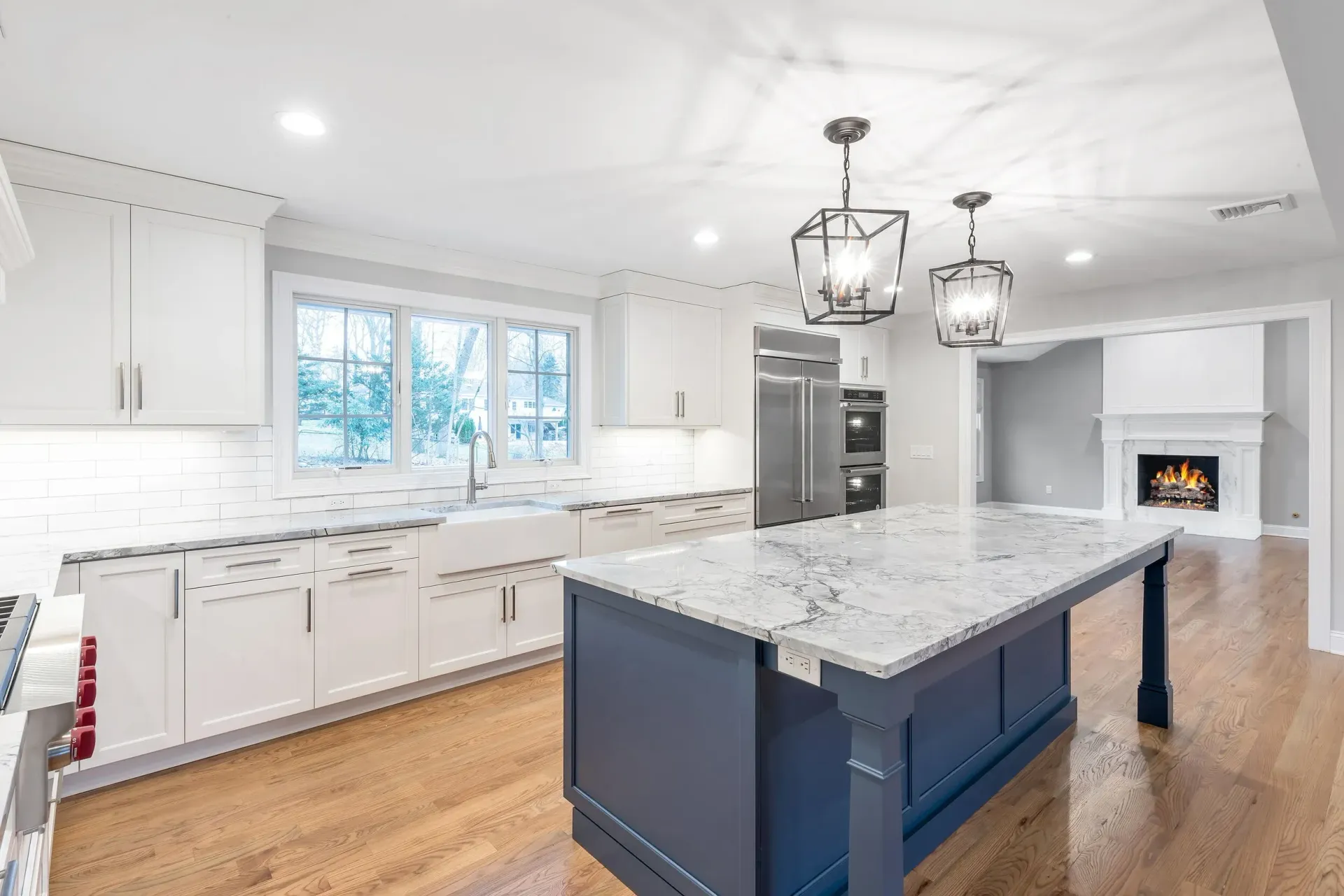 Modern kitchen with white cabinets, blue island, and granite countertops; open to living room with fireplace.
