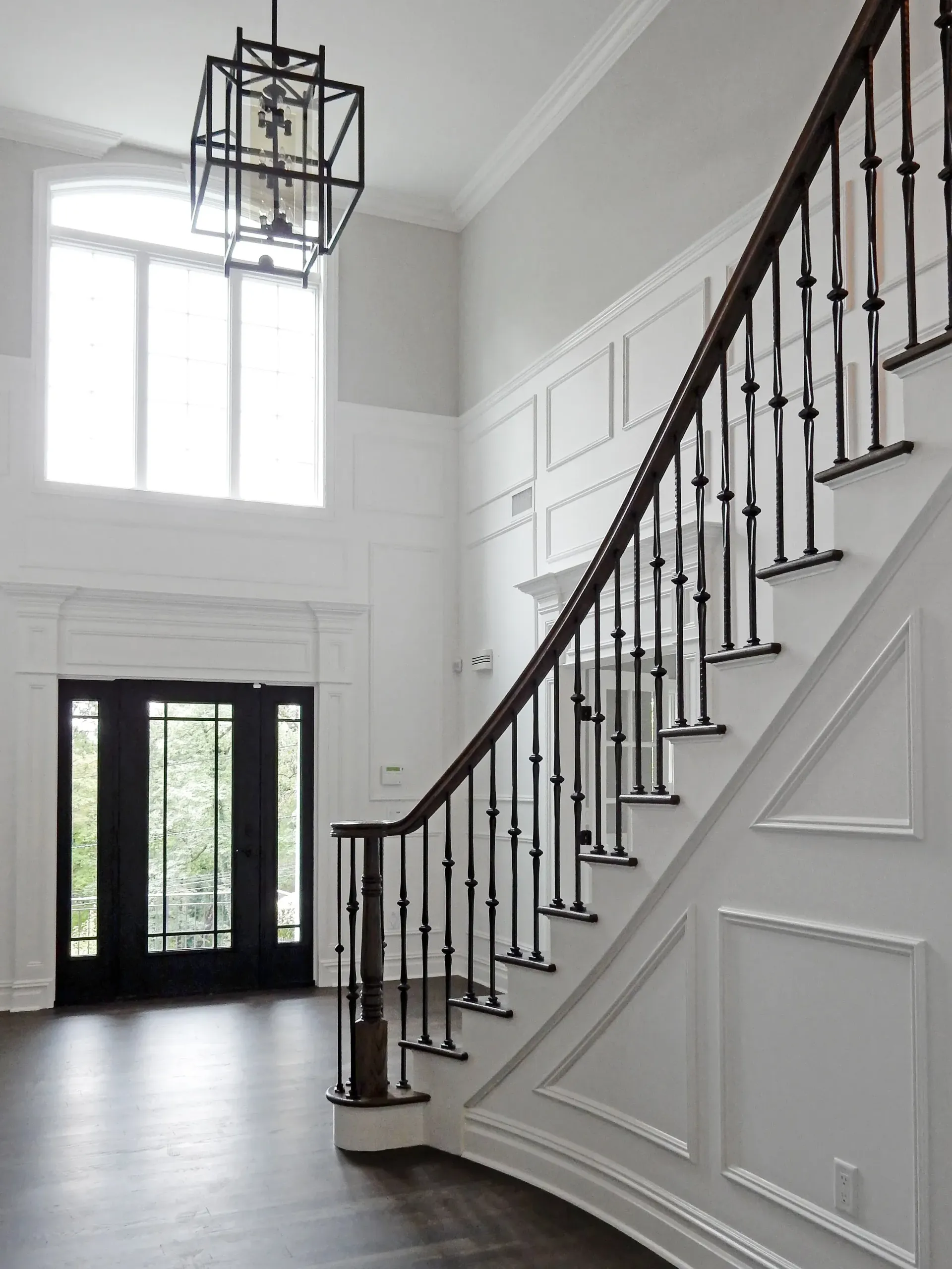Grand, bright foyer with curving staircase, black doors, and large windows.