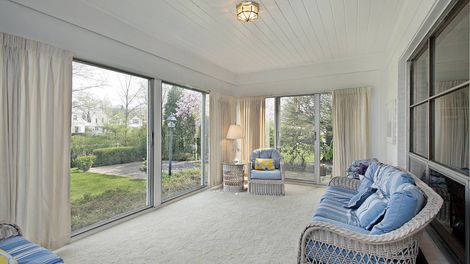 Sunroom with cream curtains, blue wicker furniture, and a view of a green yard.
