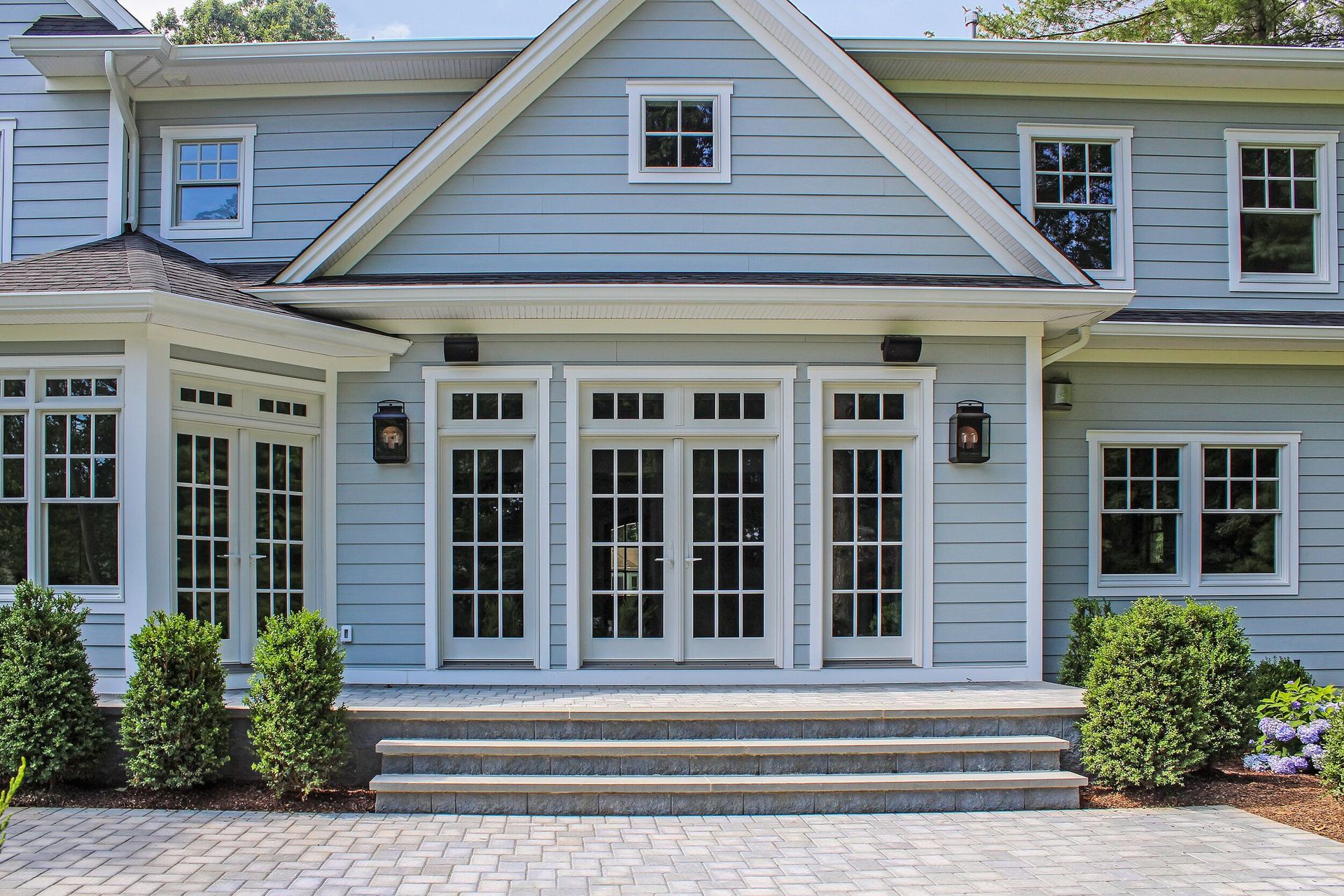 Blue house with white trim, double doors, and steps. Bushes flank the entrance.