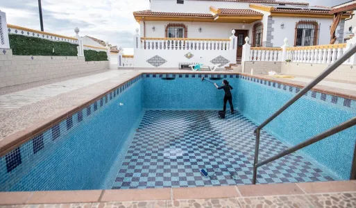 Empty backyard swimming pool with blue tiles and a person standing inside near the far wall