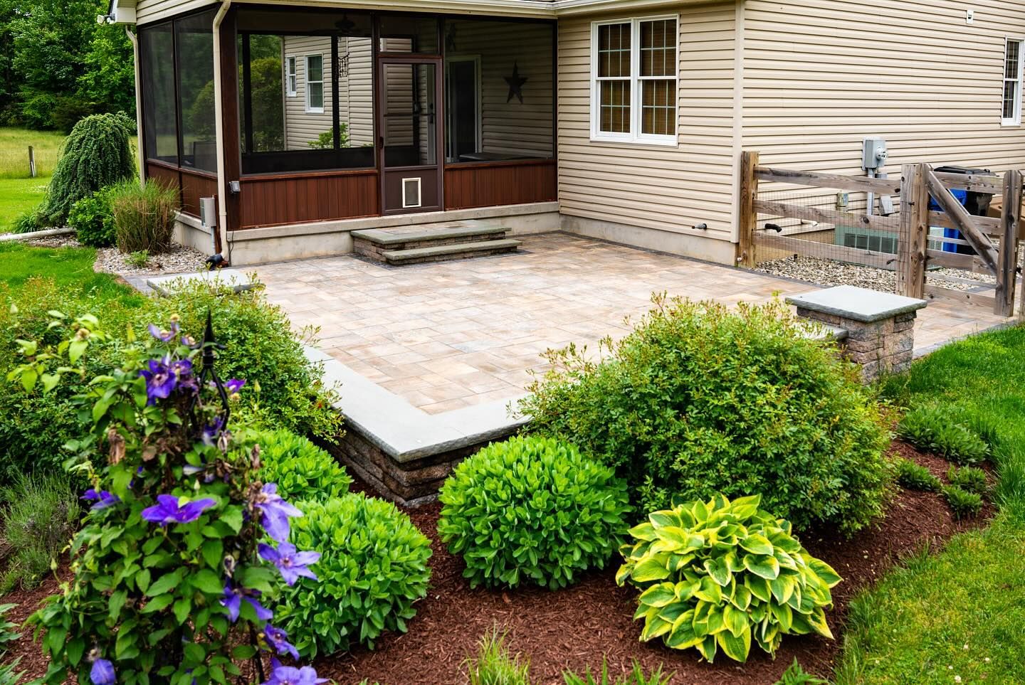 A screened in porch with a patio and flowers in front of a house.
