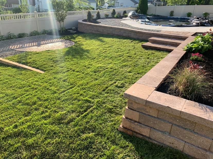 A lush green lawn with a brick wall and steps in a backyard.