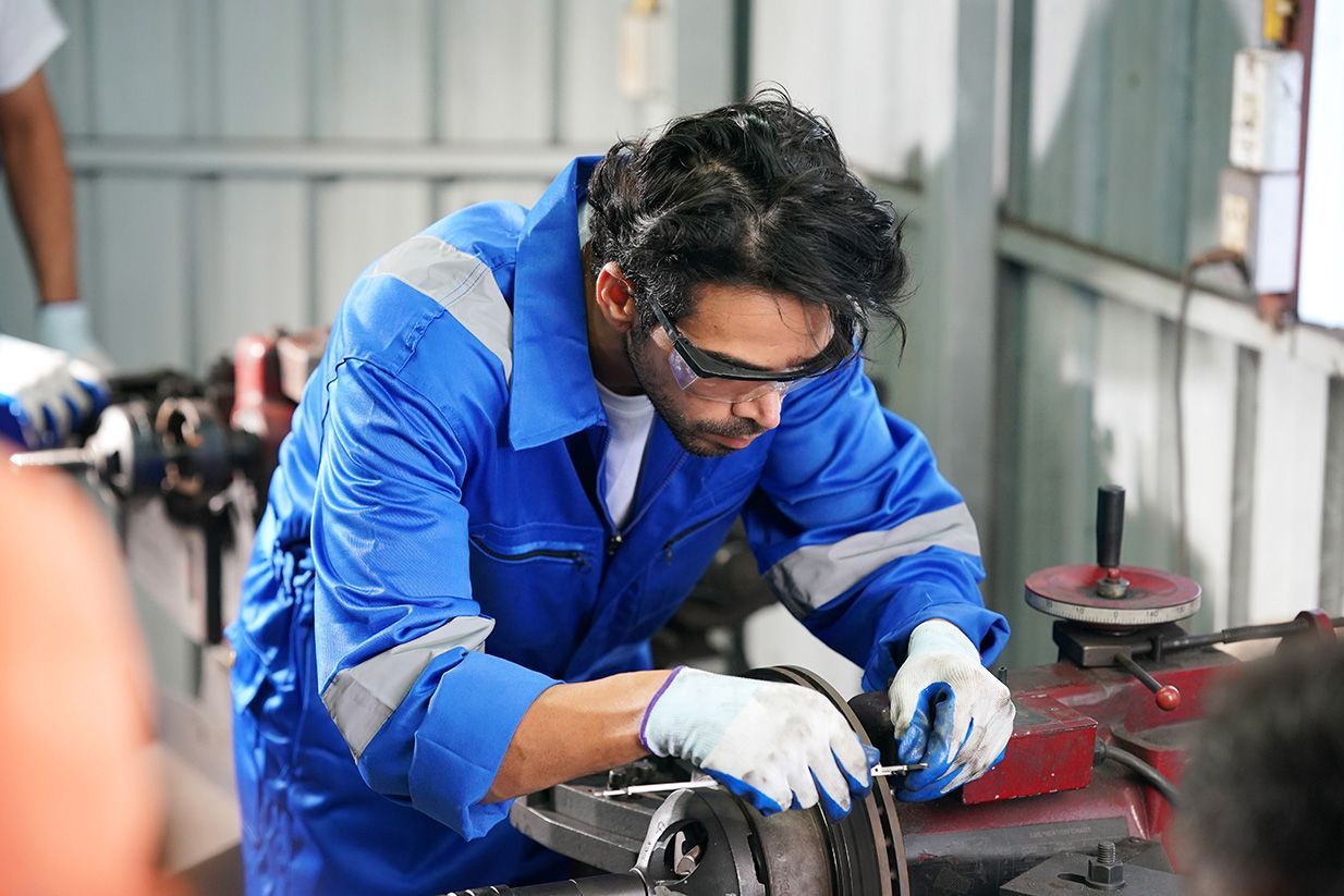Mechanic in blue coveralls and safety glasses working on machinery in a workshop.