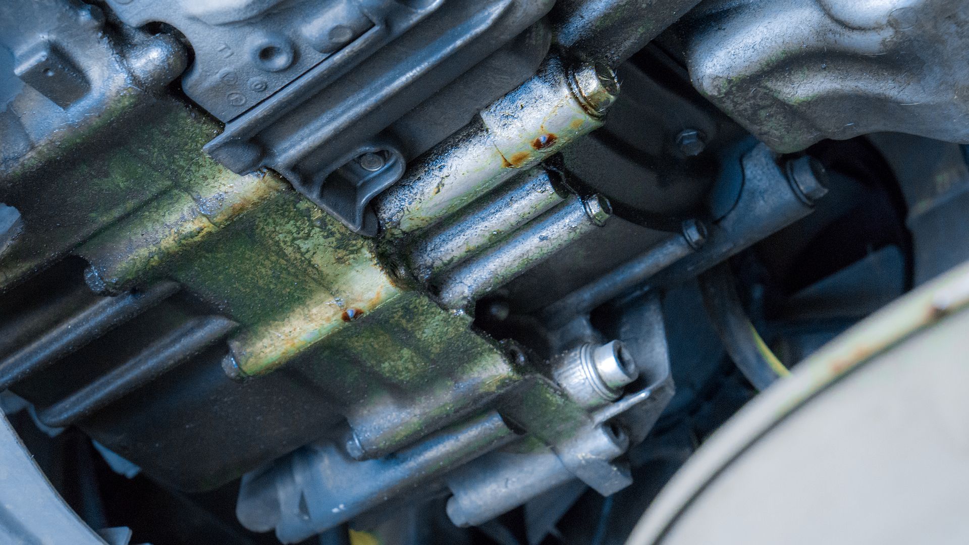 Engine underside, possible oil leak. Metallic components, dark staining, green residue visible.