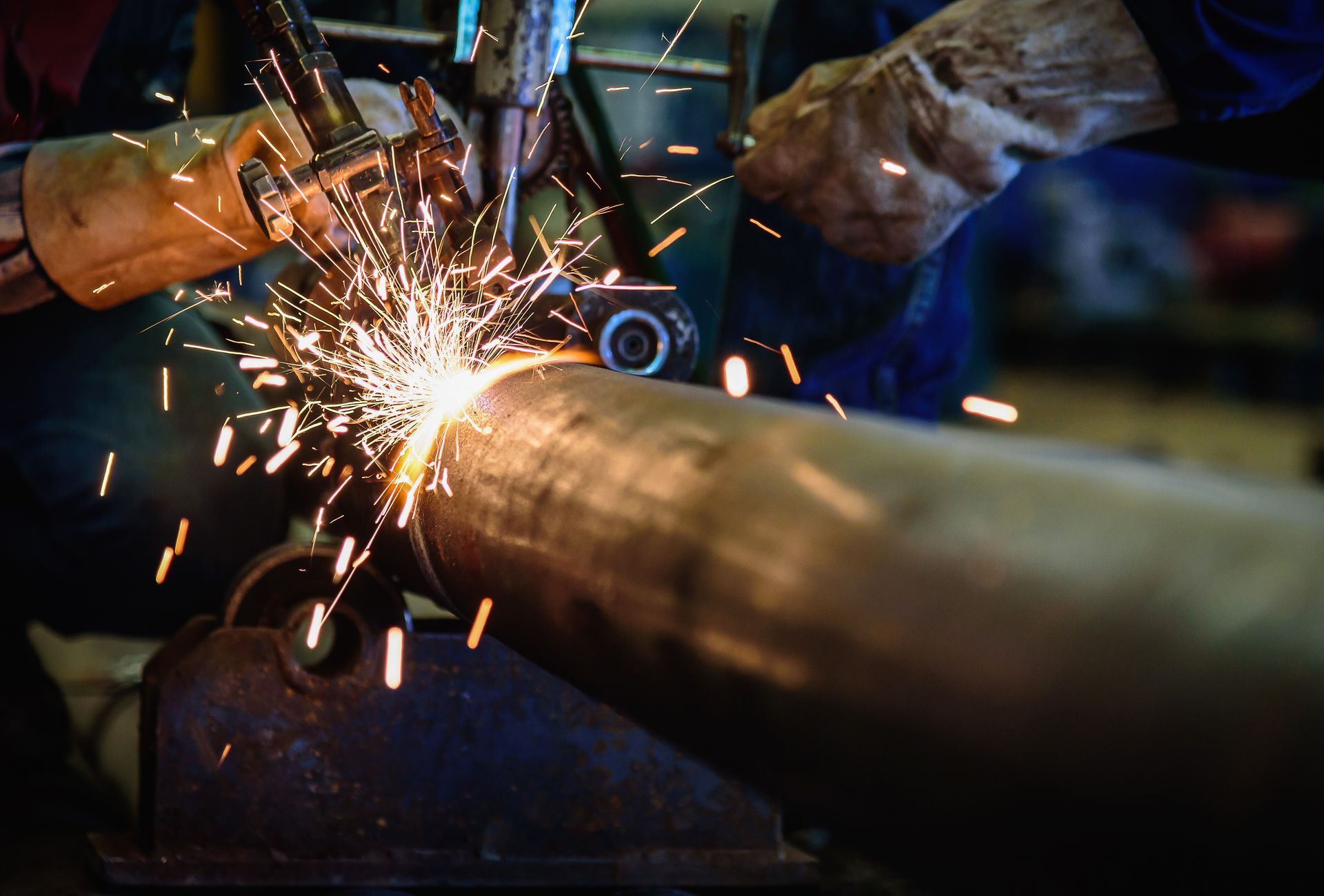 Worker grinding metal pipe with sparks flying in a dim workshop
