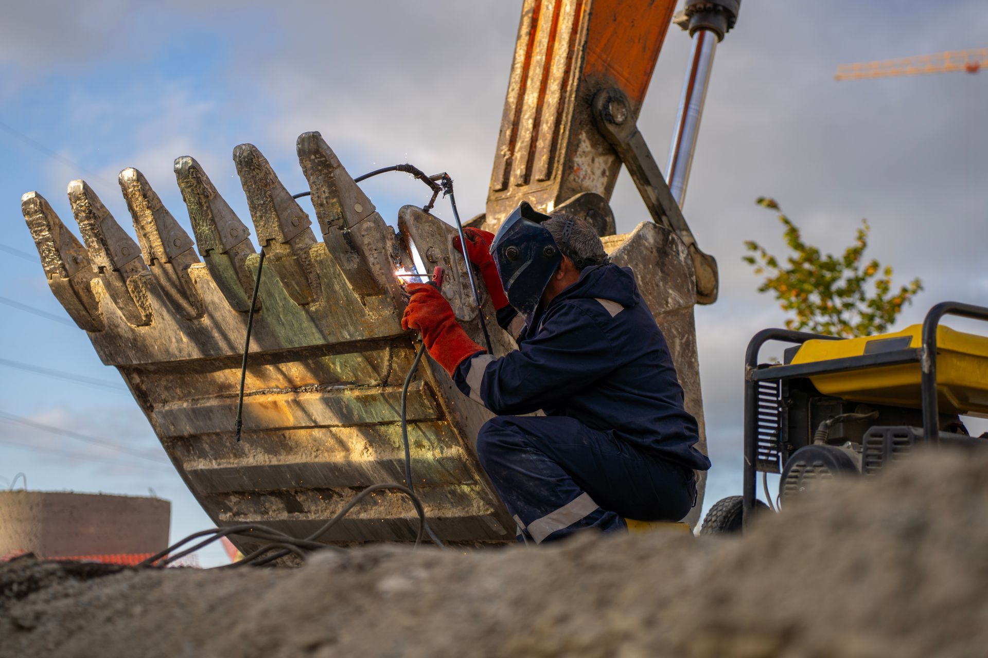 Worker using an excavator to lift a large metal bucket or grapple at a construction site
