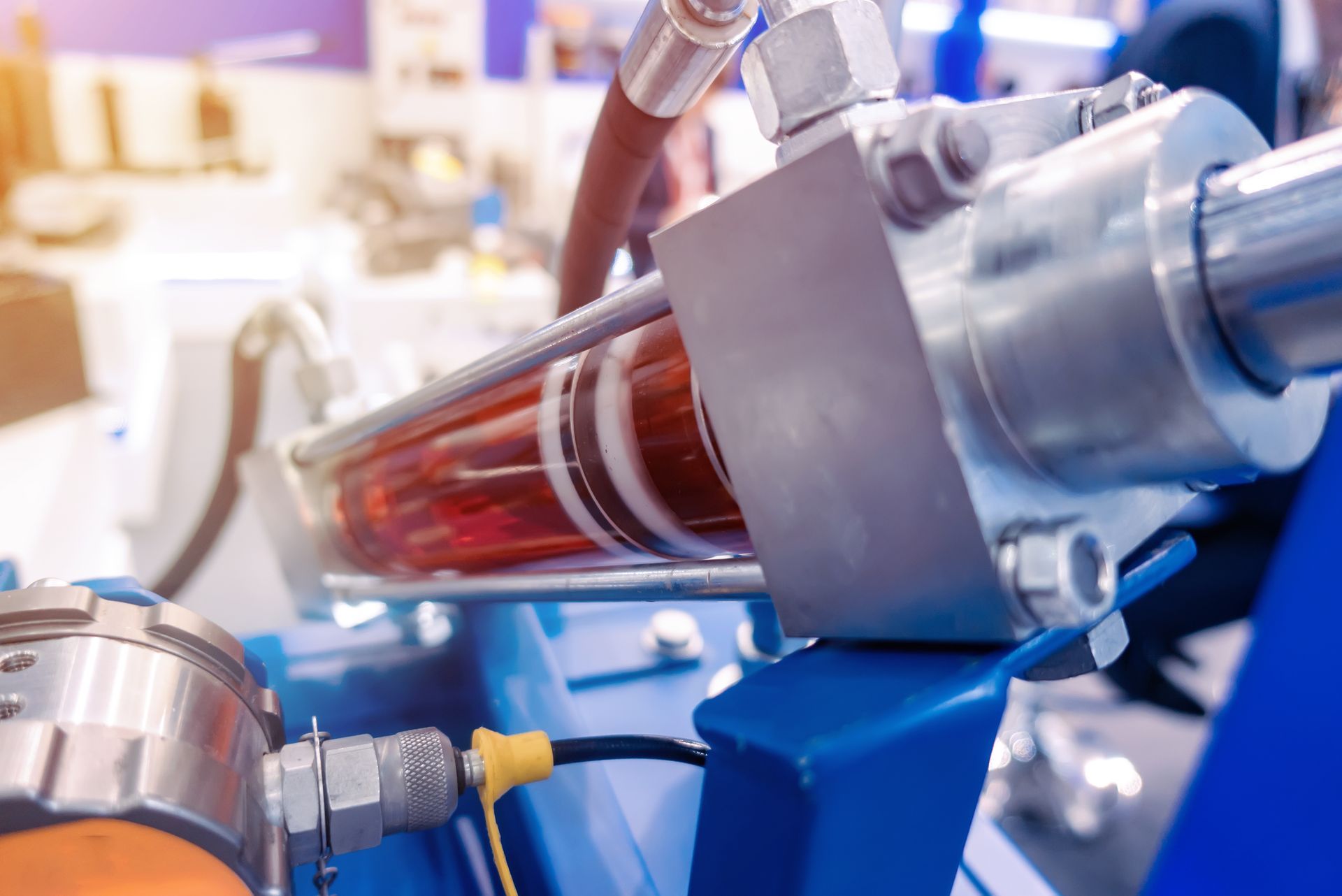 Close-up of a red fluid-filled industrial machine component with metal fittings in a factory setting