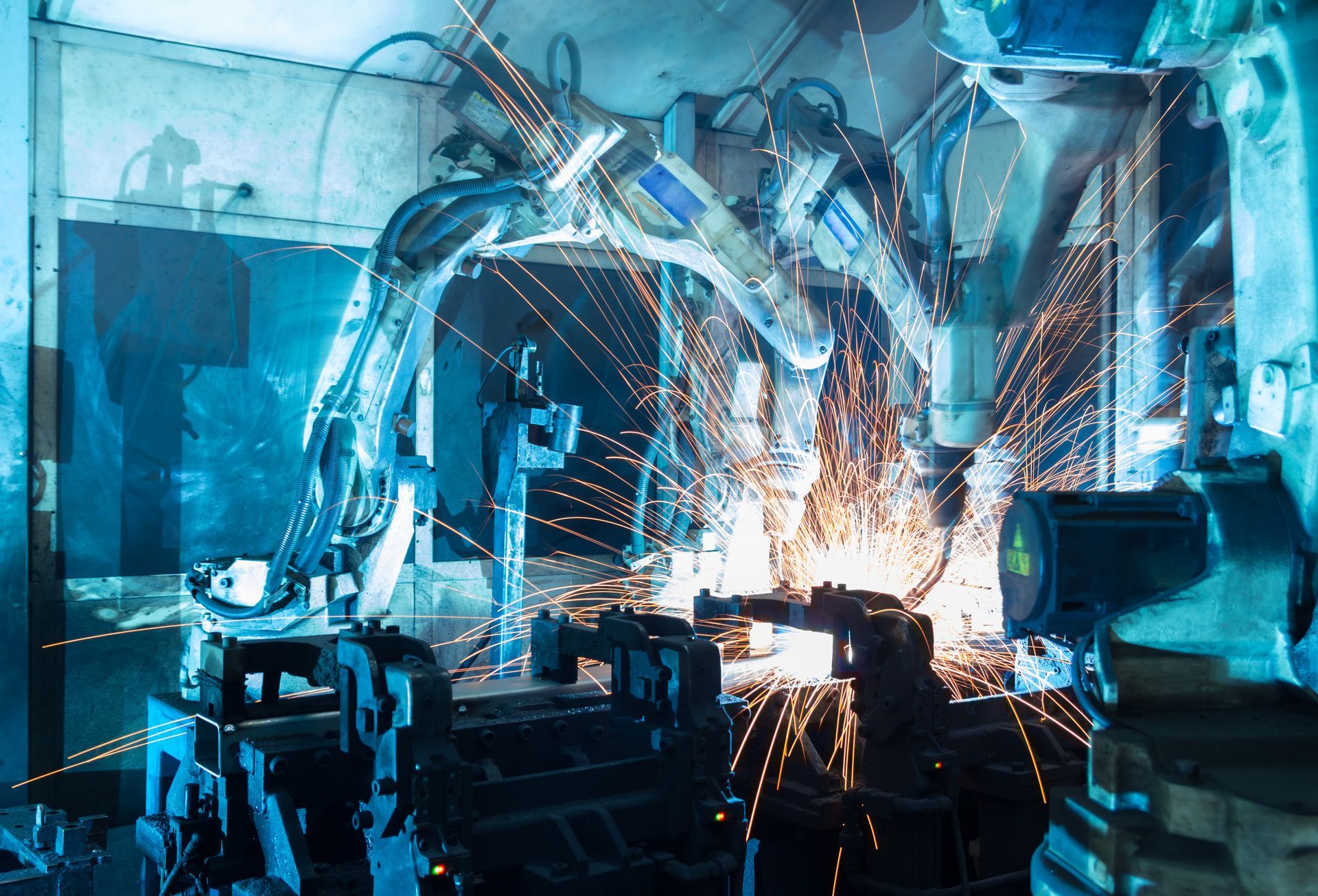 Robot welding sparks inside an industrial factory, with blue machinery and bright orange sparks