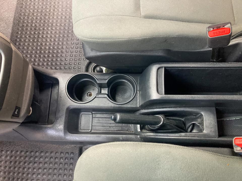 Car center console with two cup holders, storage tray, and gear selector between gray seats
