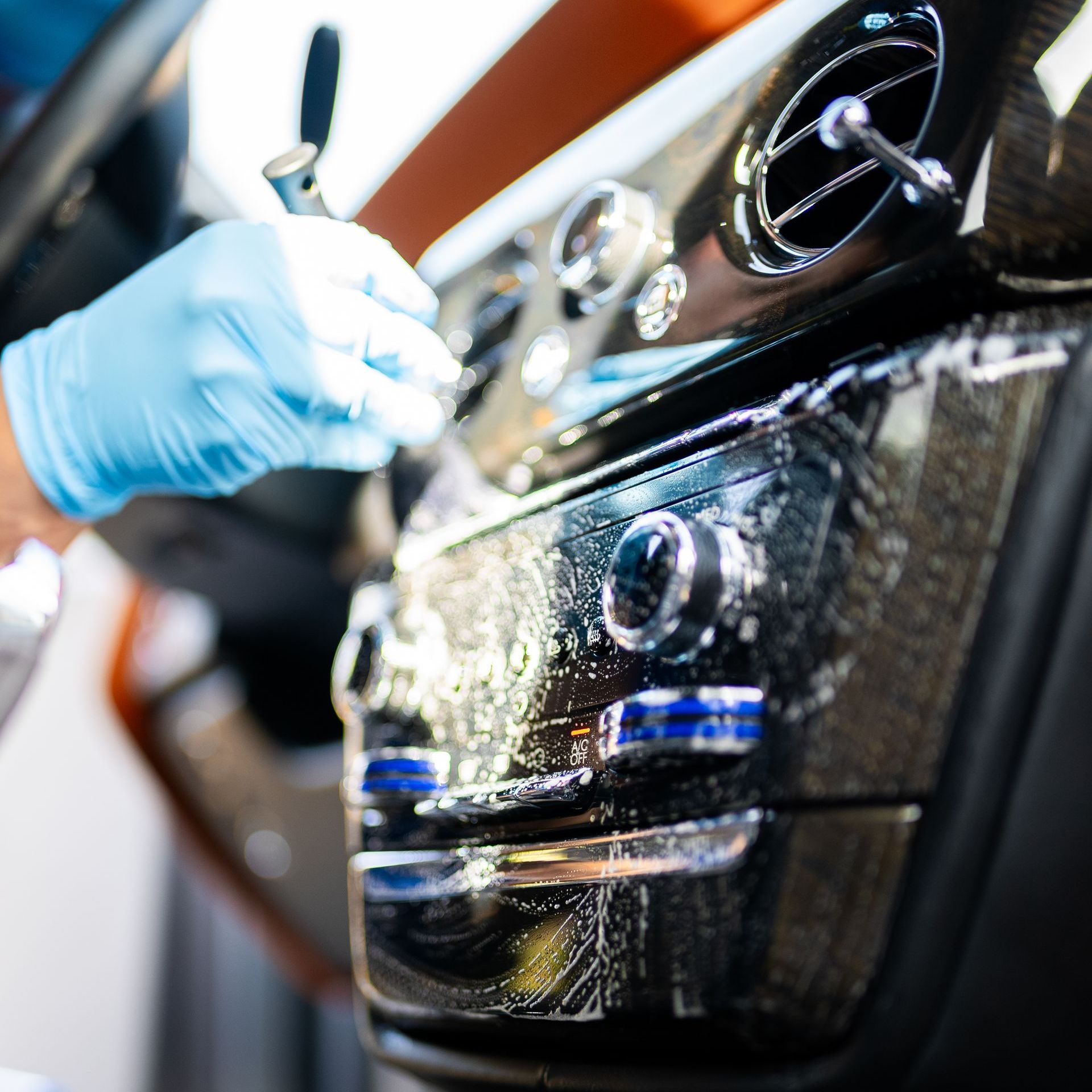 Gloved hands detailing a car's dashboard trim during a deluxe detail