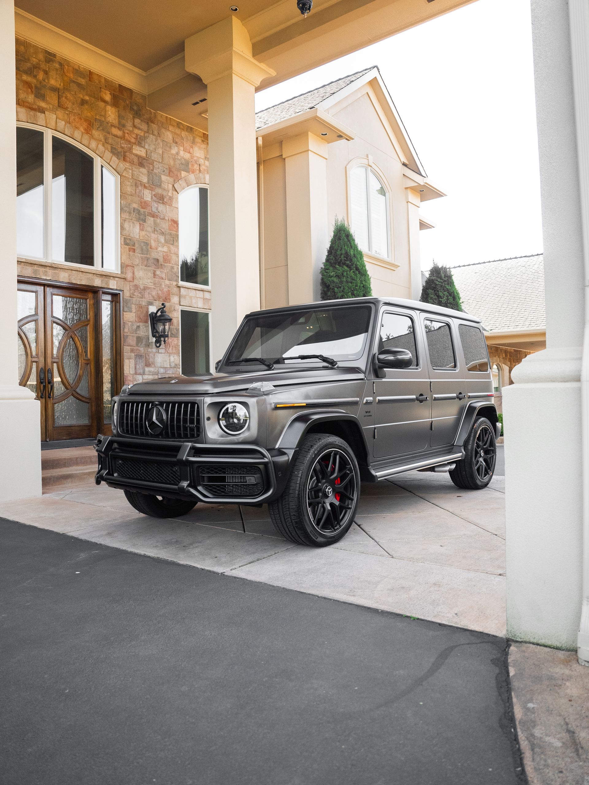 Black Mercedes G-Wagon parked under a house portico beside a stone driveway.