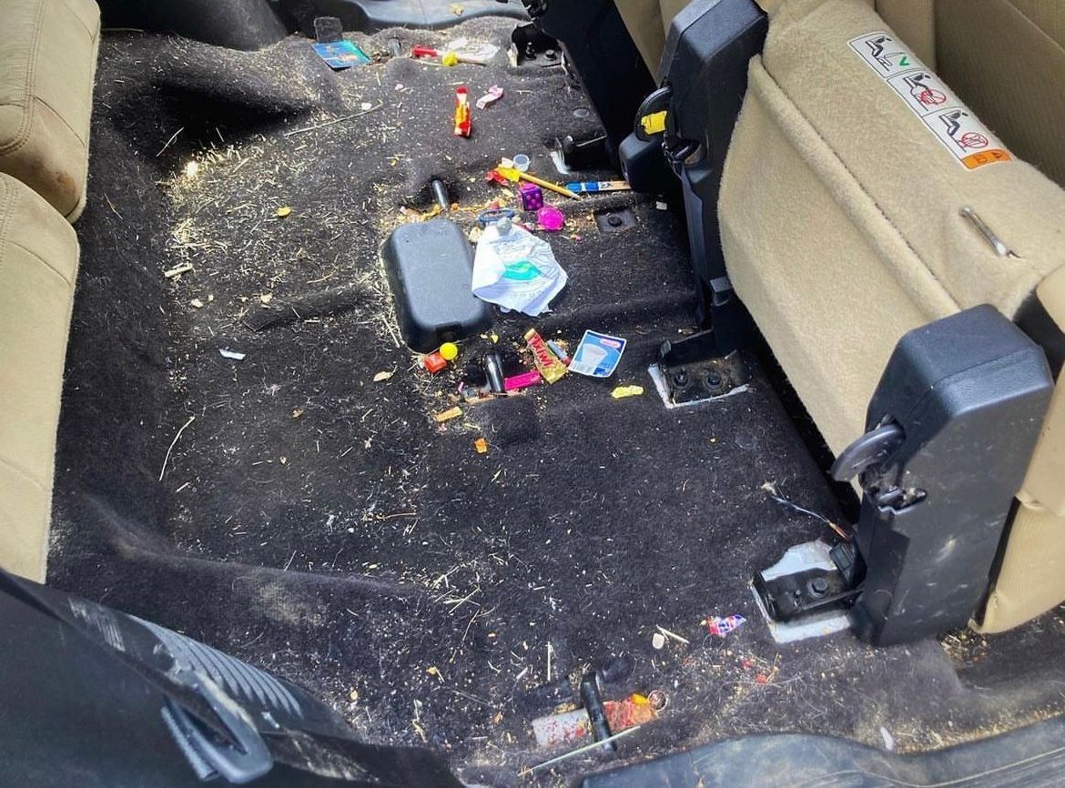 Messy car back seat with scattered trash and debris on dark upholstery