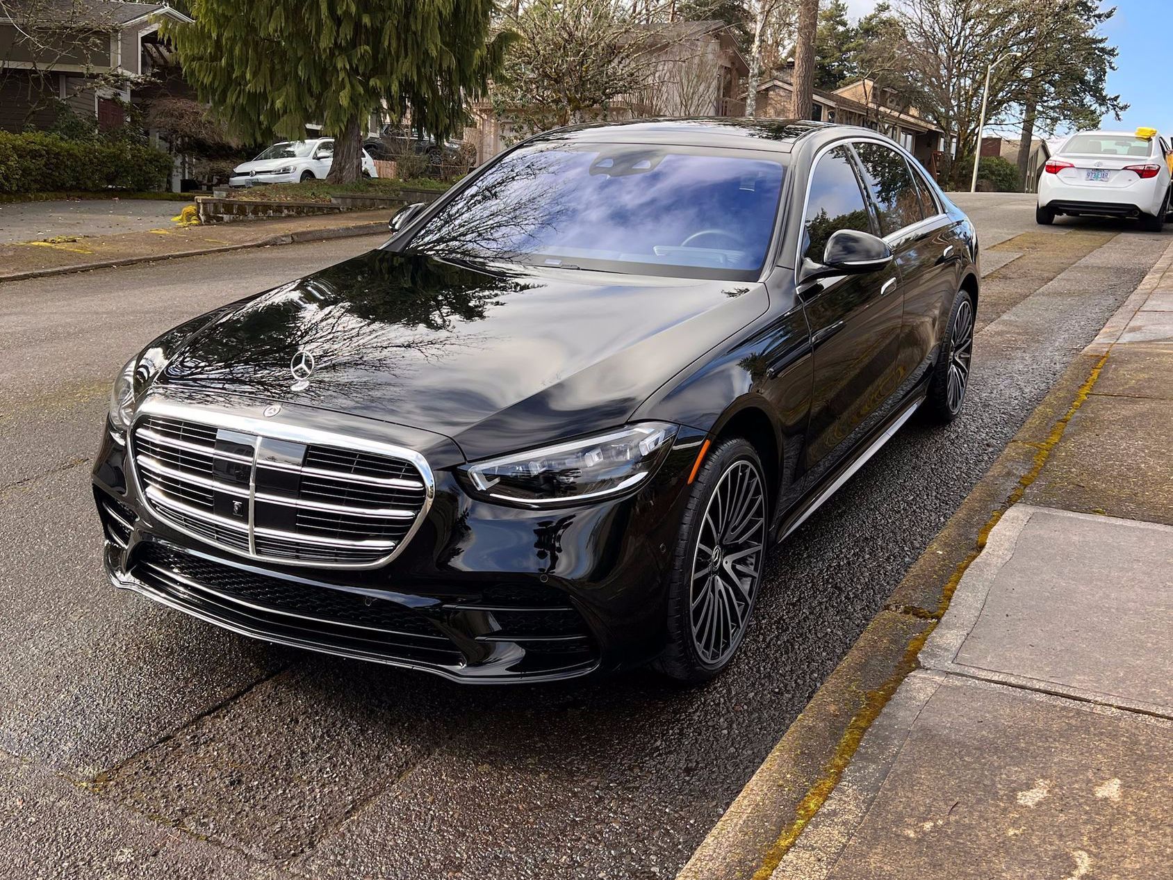 Black Mercedes sedan parked along a residential street with trees and houses in the background
