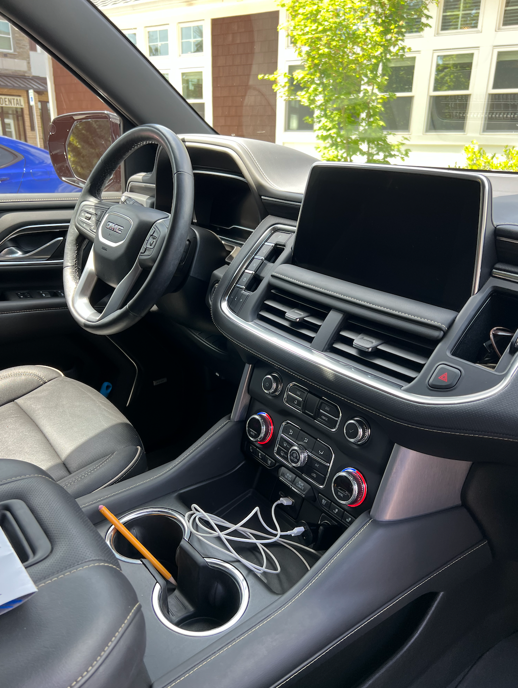Car interior with black dashboard, steering wheel, center screen, cup holders, and charging cables.