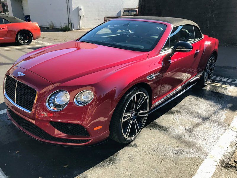 Red Bentley convertible parked in a sunlit driveway, front three-quarter view