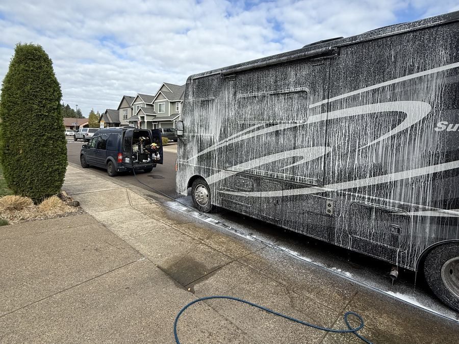 Class A motorhome covered in foam during a KeptCar mobile RV wash, with the KeptCar service van parked nearby
