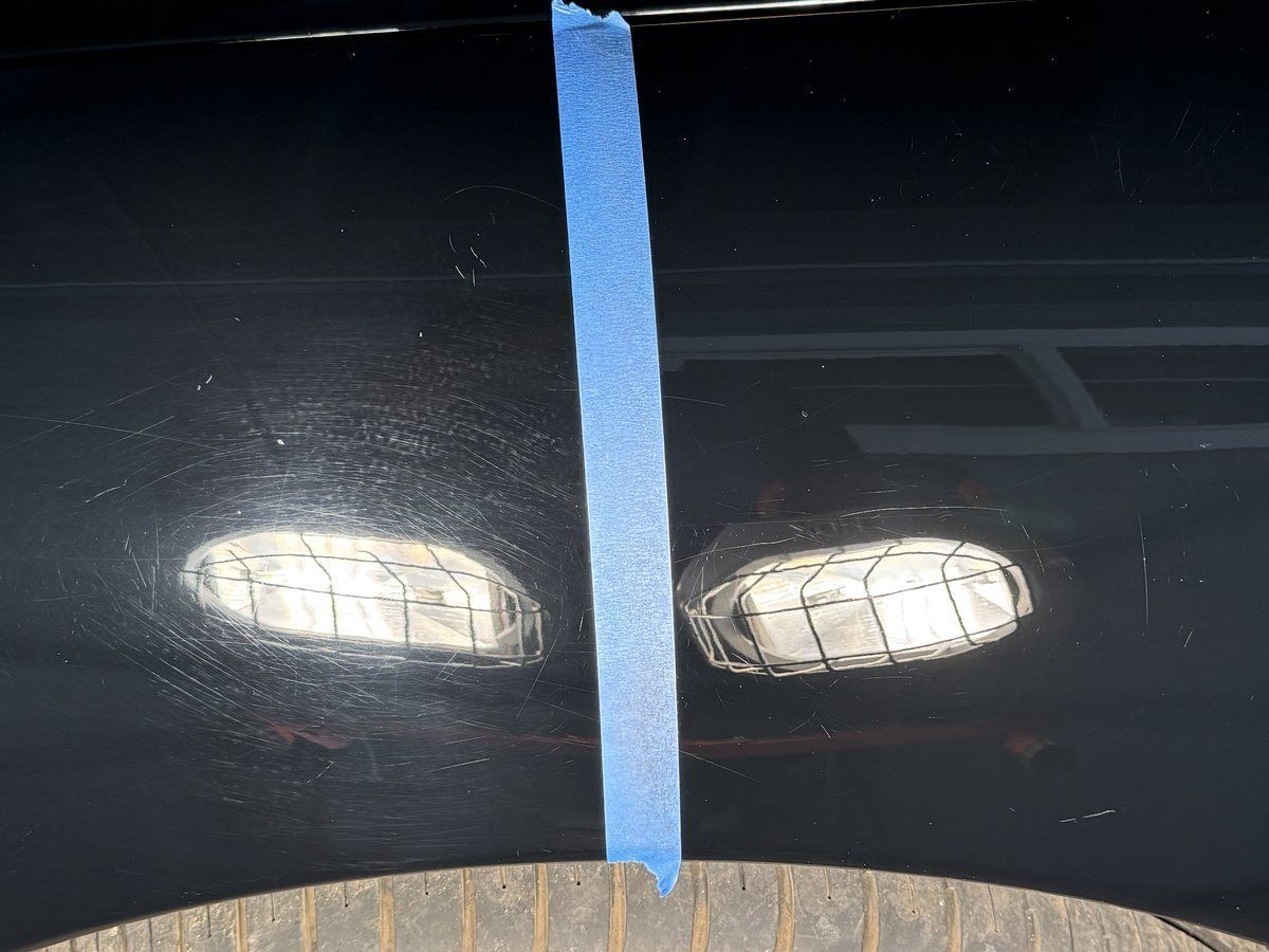 Paint correction 50/50 on a black car: swirled paint on the left of the tape, corrected mirror finish on the right