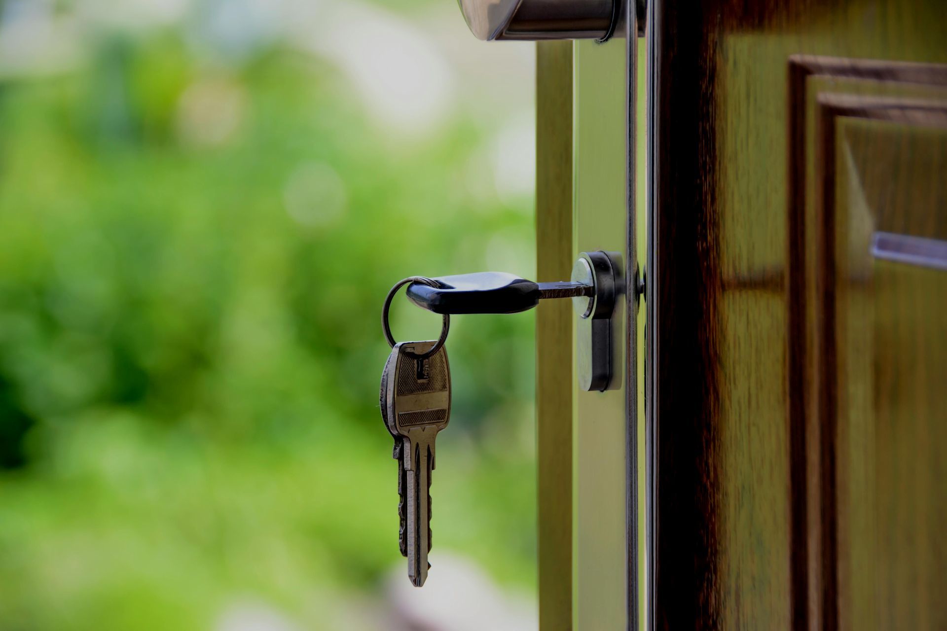 Keys hanging in a door lock with an open doorway and blurred greenery in the background
