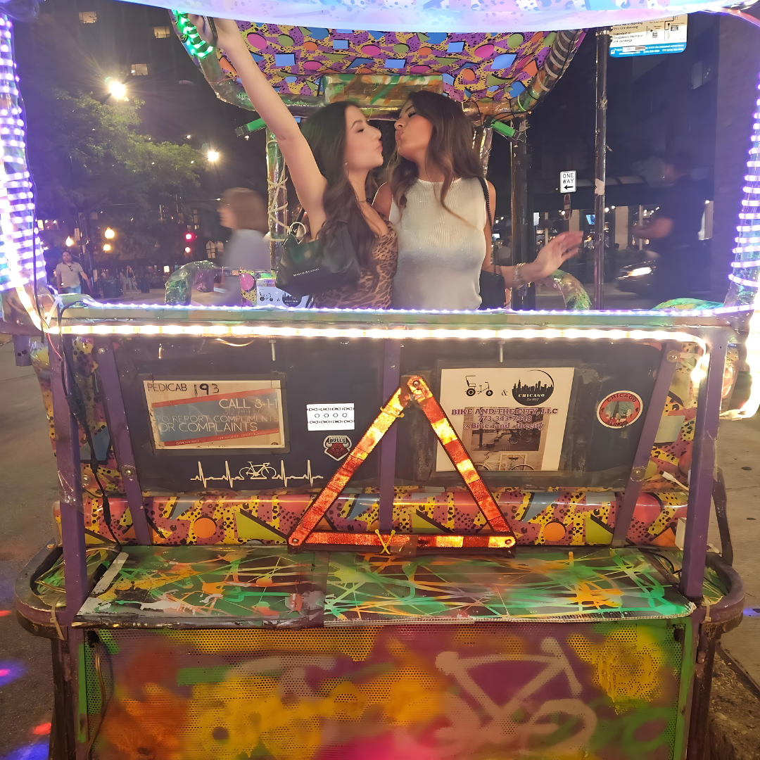 Two women enjoy a festive evening on a pedicab city tour, highlighting the fun of our illuminated chicago pedicab tours.