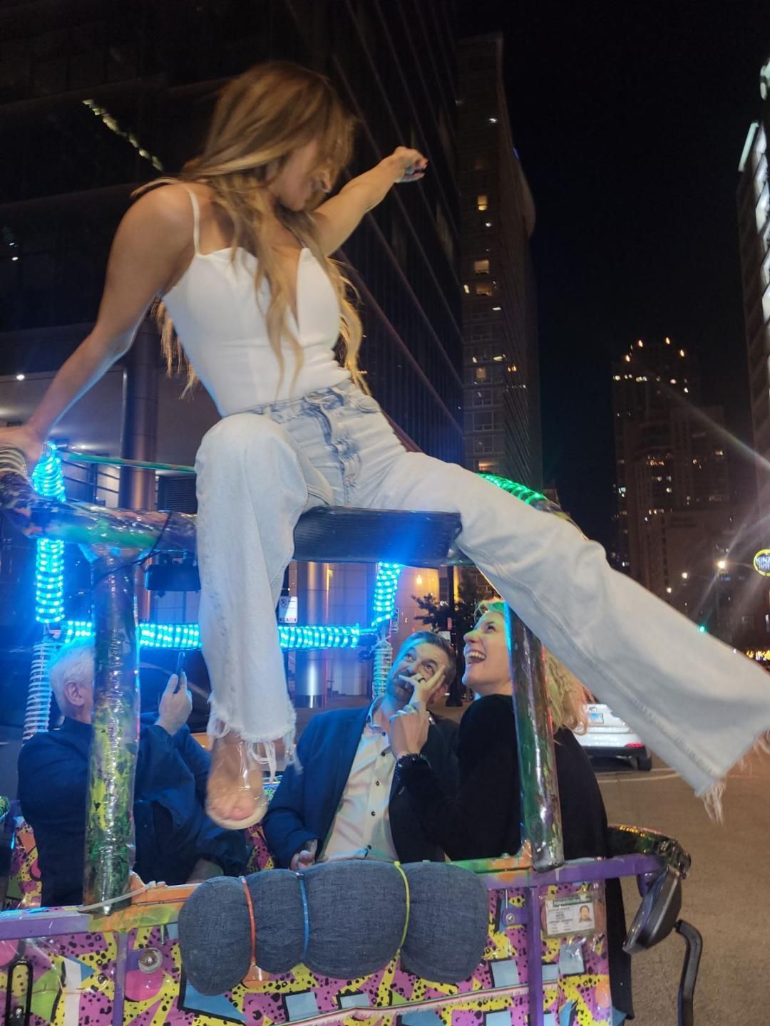 A group has a fun and energetic night out on a pedicab city tour, with a passenger playfully posing on the lighted canopy of our bike taxi chicago.