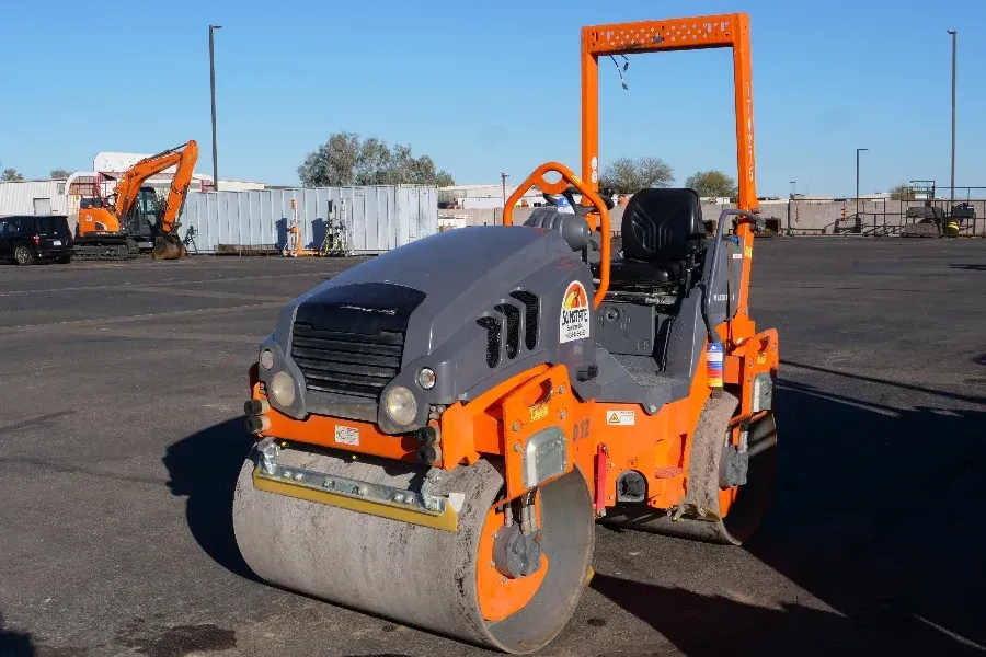 An orange and gray road roller is parked in a parking lot