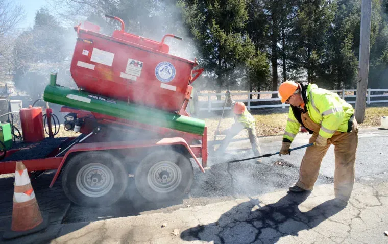 A man is working on a road next to a trailer.